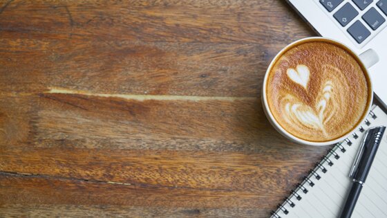 Auf einem braunen Tisch ist eine Tasse Kaffee, ein Notizblock und ein Laptop. | © Pixabay